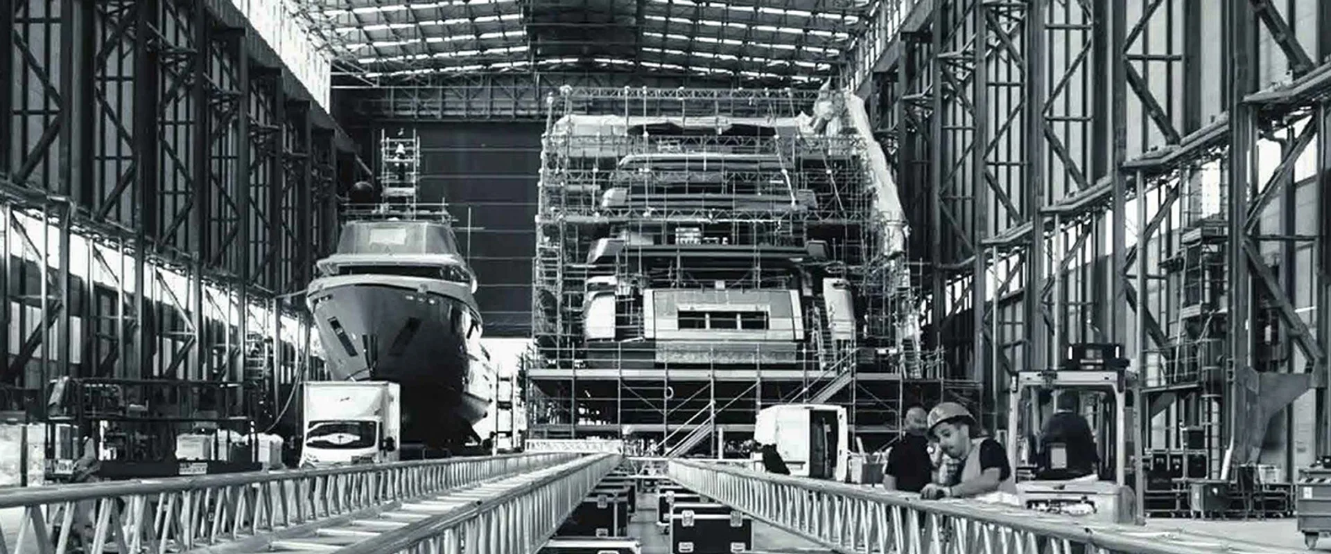 Inside a Sanlorenzo build hall — yachts under scaffolding with crew at work on the shop floor